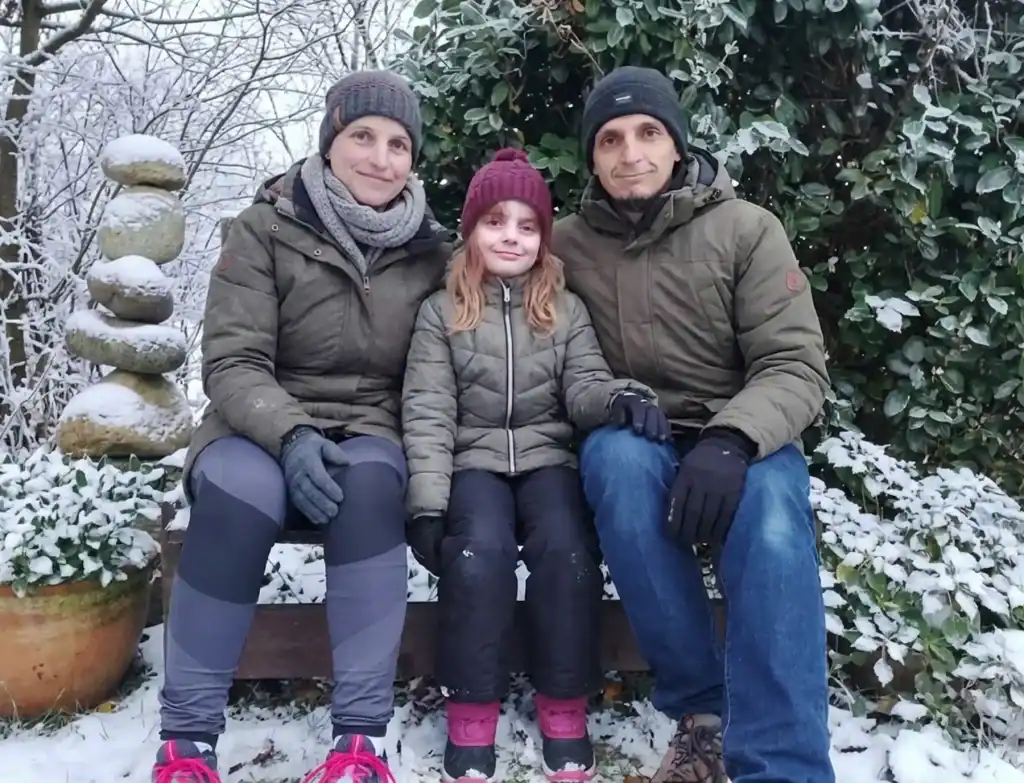 Famille Grandhaye Hiver souriante assise sur un banc dans un jardin enneigé